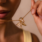 A woman, dressed in a yellow top, holds the Angel Wing Charm in 18K Gold—a necklace featuring pavé-set wings and jeweled charms—close to her lips.