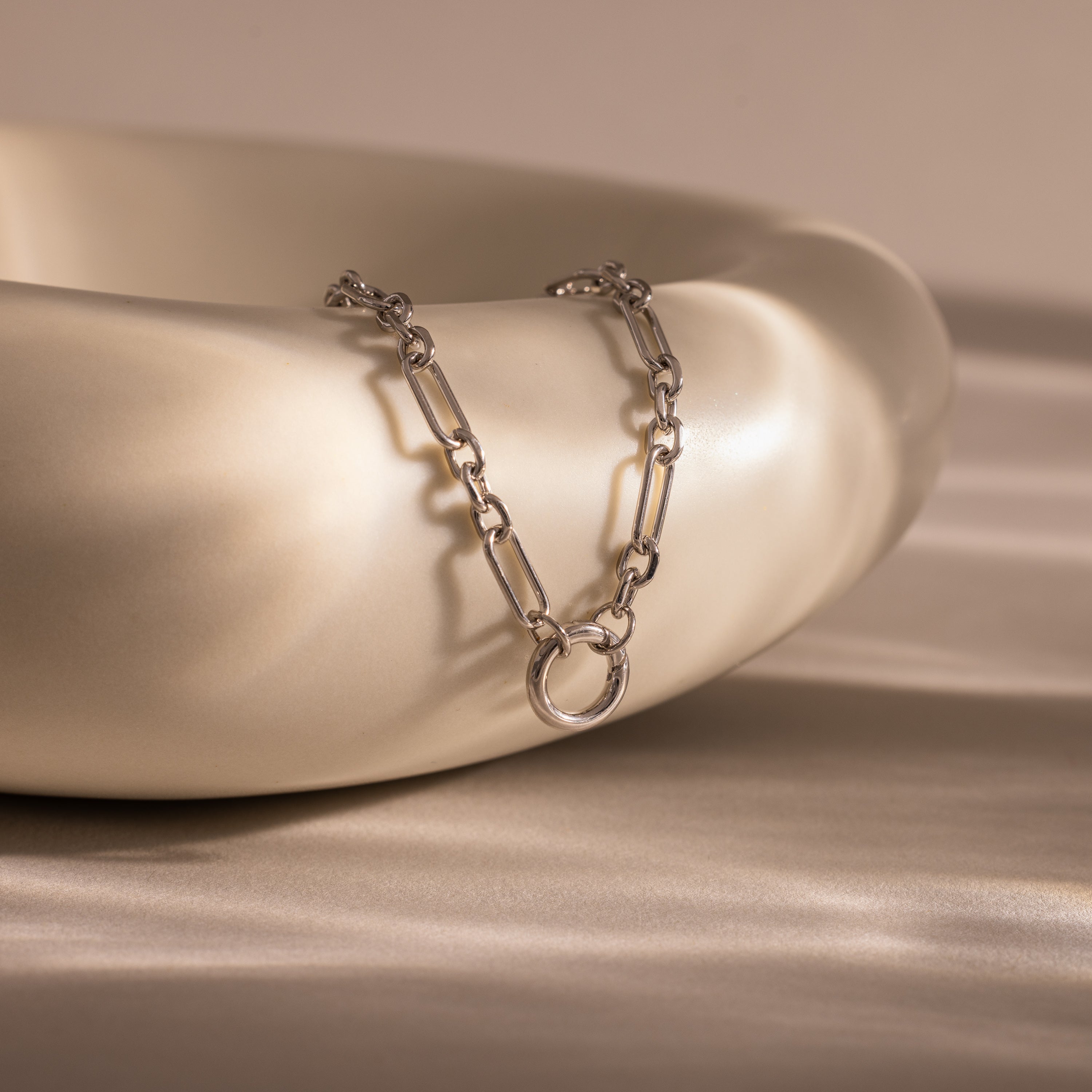 Rolo Circle Figaro Necklace in Silver featuring a round pendant and elegant link design, displayed draped over a smooth, cream-colored ceramic bowl.