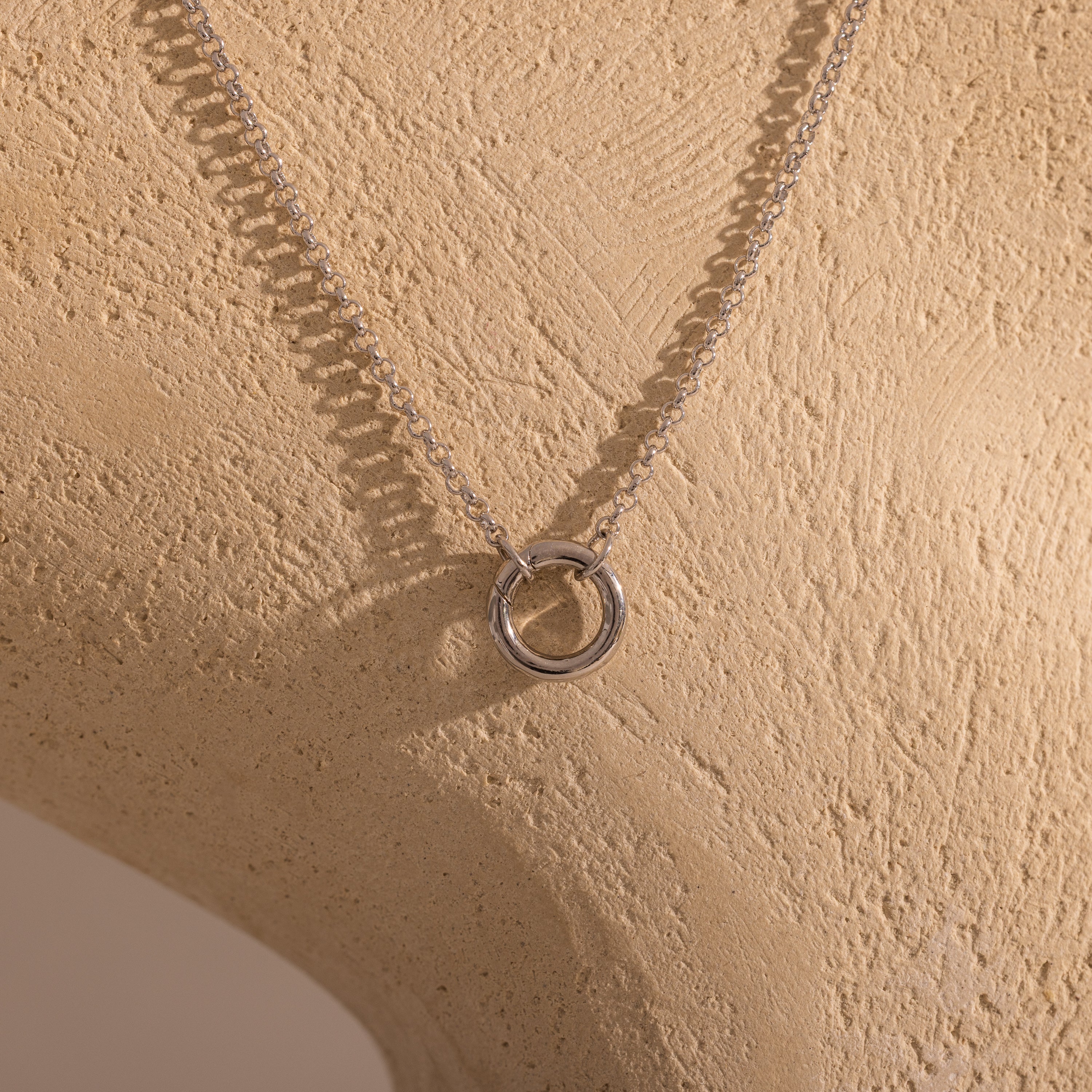 The Cable Circle Charm Necklace in Silver features a circular pendant, ideal for layering or wearing as a statement piece, and is displayed on a beige textured mannequin bust.