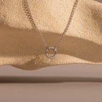 The Cable Circle Charm Necklace in Silver features a circular pendant, displayed against a textured beige rock background—ideal as a statement piece or for layering with your favorite necklaces.