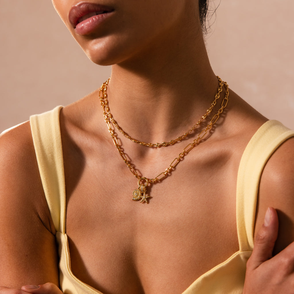 Woman in yellow top shown from shoulders to lips, wearing the Rolo Circle Figaro Necklace in 18K Gold layered with gold chains and charms, including a statement front clasp.