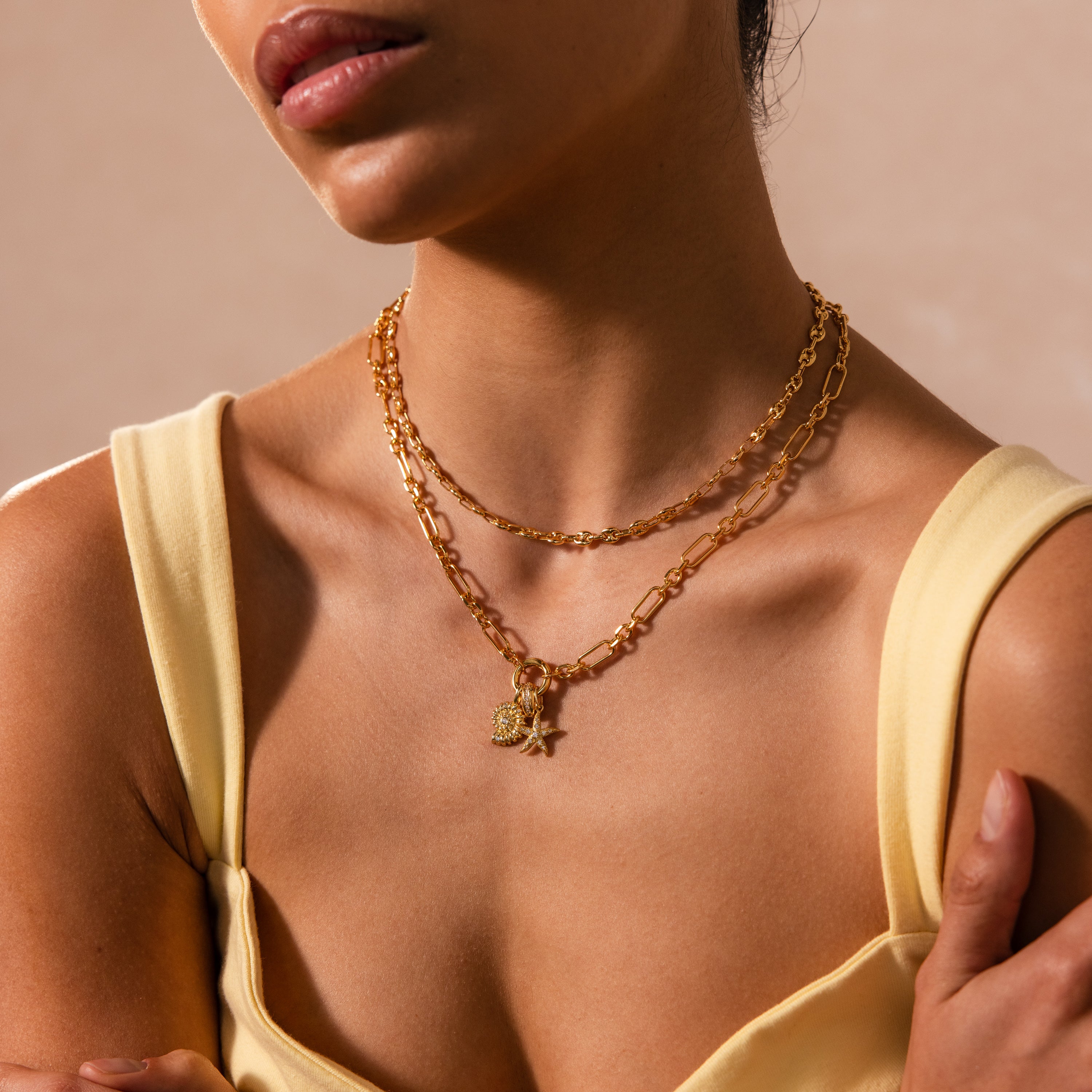 Woman in yellow top shown from shoulders to lips, wearing the Rolo Circle Figaro Necklace in 18K Gold layered with gold chains and charms, including a statement front clasp.