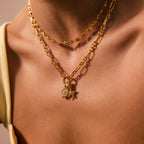 Close-up of a woman wearing two gold chain necklaces—a classic link with star and leaf charms, and the Rolo Circle Figaro Necklace in 18K Gold—against bare skin.