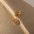The Star Opal Hand Charm earring features a hand holding a star and opal stones, symbolizing intuition and cosmic energy, shown on a textured beige surface.