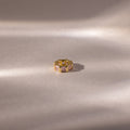 The Infinity Princess Pink Tourmaline Charm, featuring pink gem insets and delicate princess-cut stones, rests on a soft, light beige satin surface with gentle shadows.