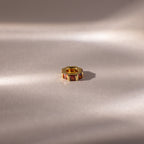 The Infinity Princess Garnet Charm, adorned with princess-cut stones and red garnet accents, rests on a softly lit, light-colored surface.