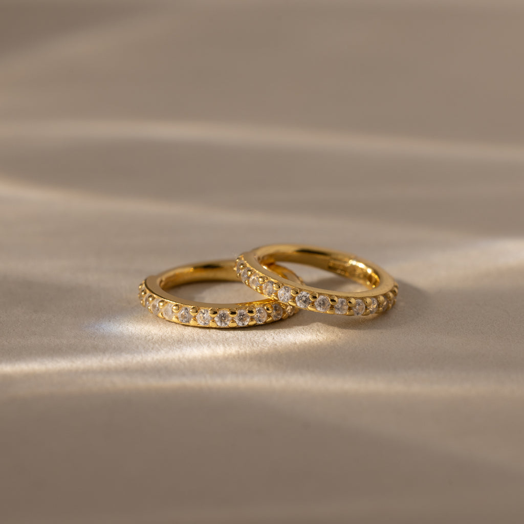 Two Diamond Clicker Huggies with small diamonds rest on a soft, beige surface in gentle light—perfect for pairing with your favorite everyday earrings.