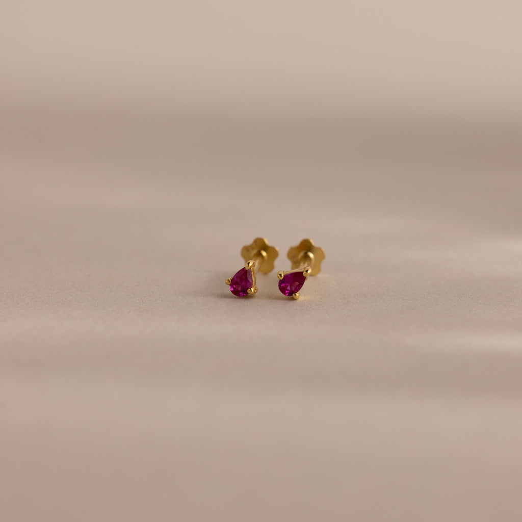 Teardrop Ruby Flatback Studs are shown against a soft, neutral background. These elegant gold earrings feature pink teardrop gemstones, making them a perfect birthstone gift for birthdays.