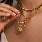 A hand displays a gold necklace with several charms, featuring the Teardrop Blue Zircon Charm in a gold bezel setting; layered gold chains accent the look.