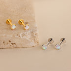 Opal Flat Back Studs in Sterling Silver feature iridescent stones and are displayed on beige stone. These comfortable earrings offer everyday elegance.