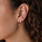 Close-up of a woman's ear with the Classic Diamond Earrings Set in Sterling Silver, which pairs beautifully with her curly brown hair—an elegant wedding jewelry choice.