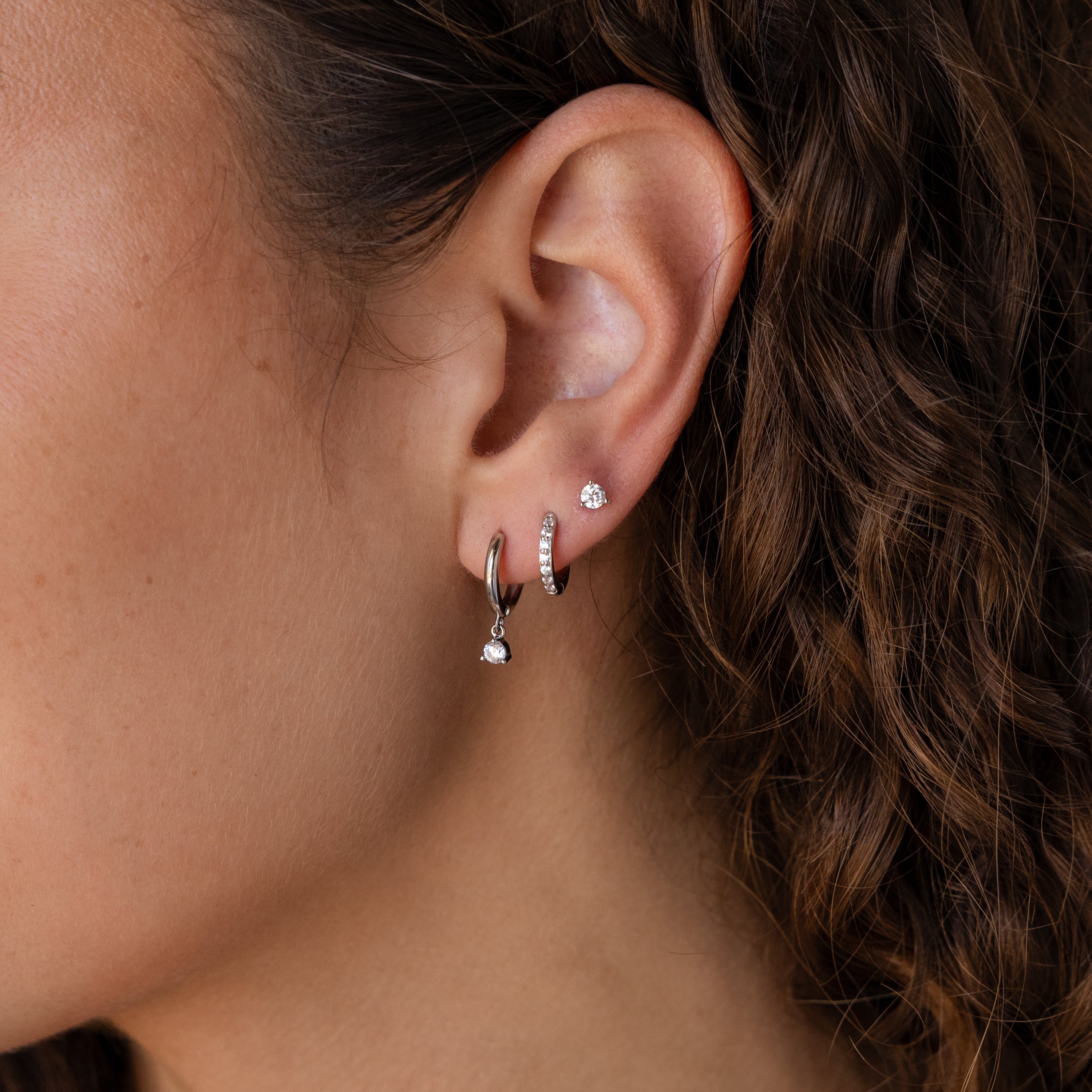Close-up of a woman's ear with the Classic Diamond Earrings Set in Sterling Silver, which pairs beautifully with her curly brown hair—an elegant wedding jewelry choice.