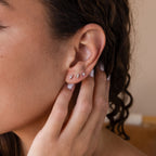 Close-up of a person touching their ear, wearing three Tiny Diamond Flatback Studs Set in Sterling Silver in the earlobe.