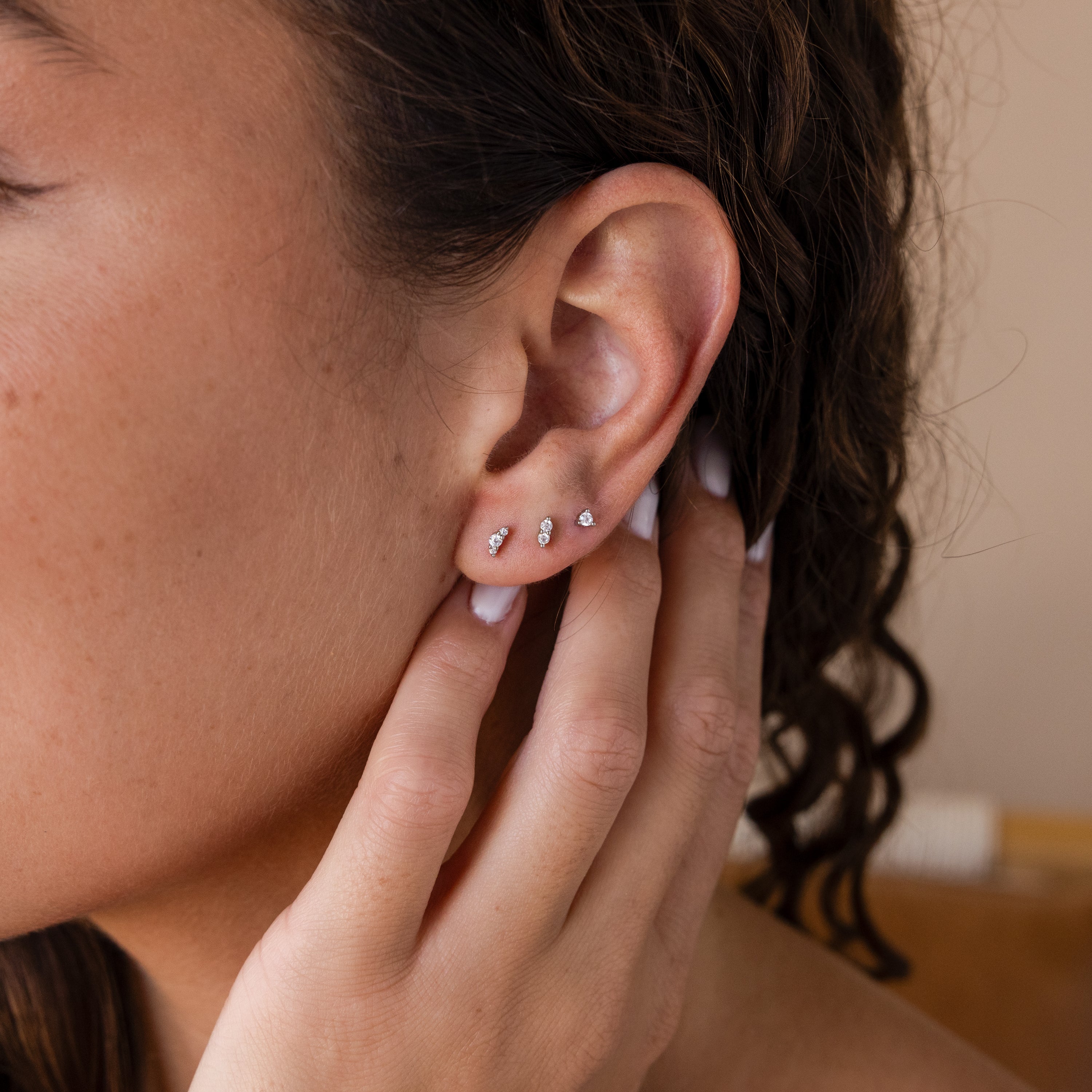 Close-up of a person touching their ear, wearing three Tiny Diamond Flatback Studs Set in Sterling Silver in the earlobe.