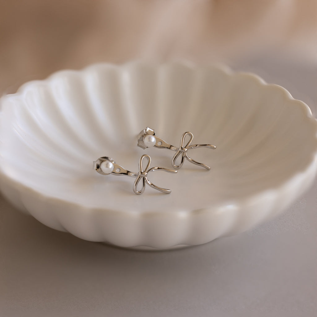 Pearl & Bow Ear Jackets in Sterling Silver shown with pearl studs on a white scalloped dish.