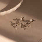 The Pearl & Bow Ear Jackets in Sterling Silver feature delicate pearl accents in a unique bow design, resting elegantly on a neutral surface near a white ceramic dish.