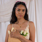 Woman with long dark hair and a pink bow holds a straw bag filled with white tulips, wearing the Heart Link Chain Necklace, against a soft fabric backdrop.