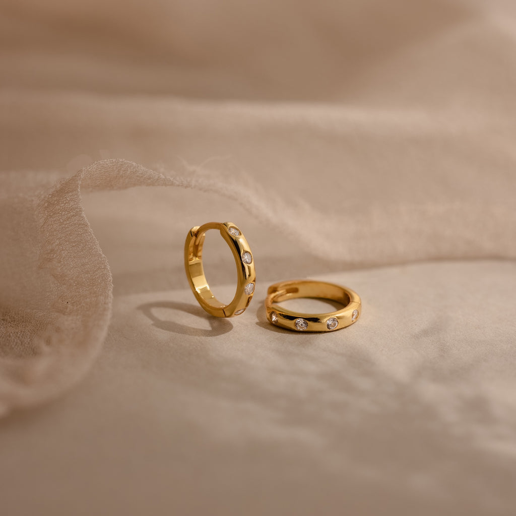 Two Mini Diamond Sprinkle Huggies with sparkling diamonds are shown on soft beige fabric under gentle lighting.