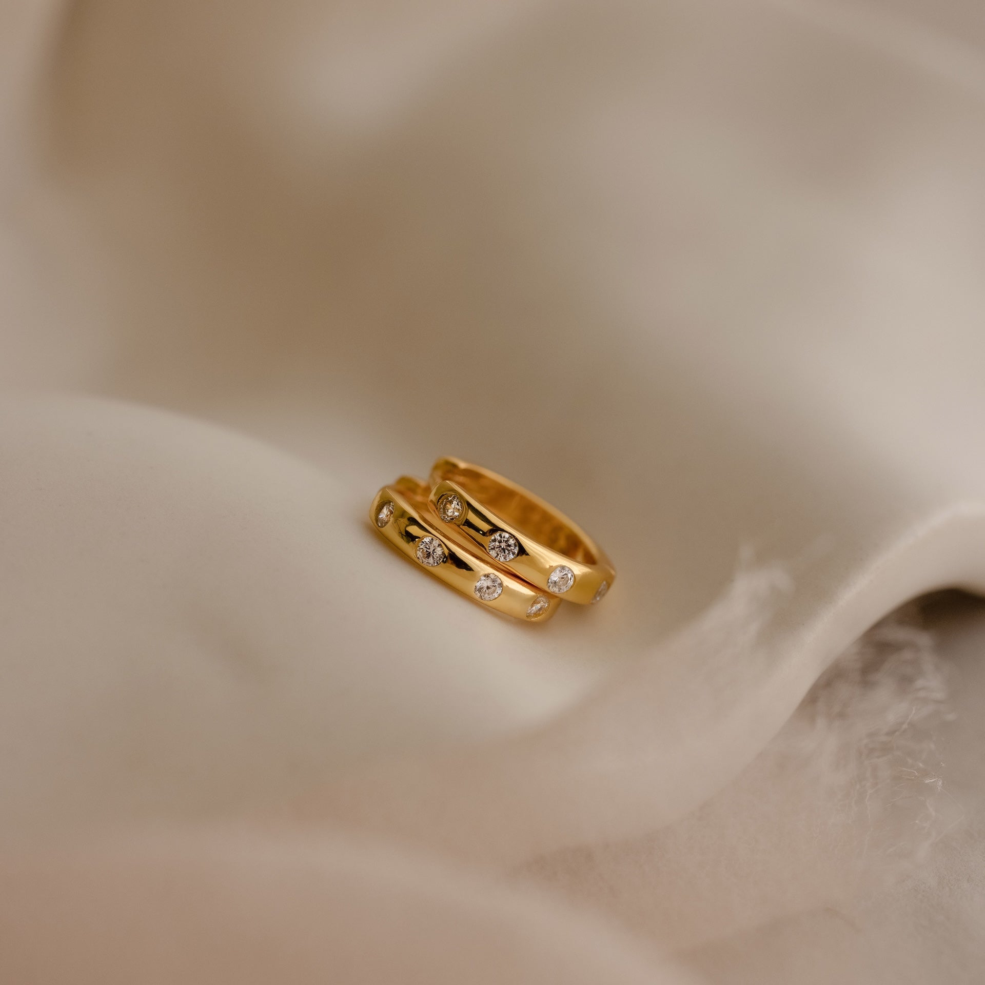 Mini Diamond Sprinkle Huggies in 18K Gold shine with sparkling diamonds, displayed on soft beige fabric.