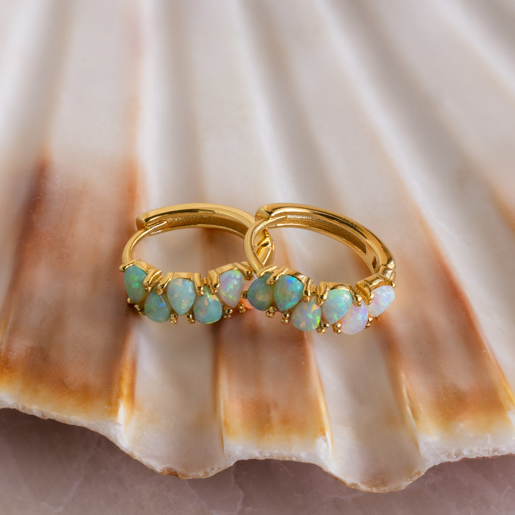 The Ombre Opal Huggies in 18K Gold, featuring green teardrop opal accents, rest on a scallop seashell to highlight their vibrant beauty.