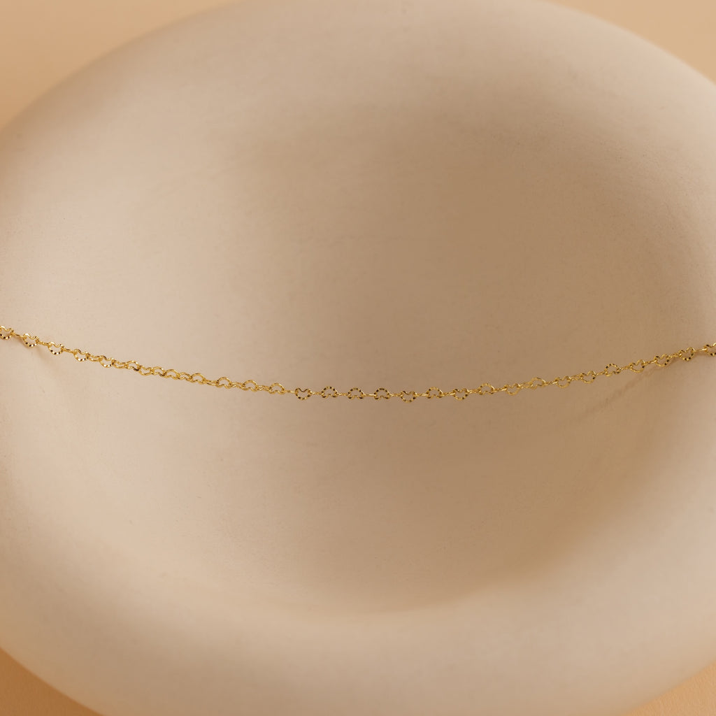 Heart Link Chain Necklace in 18K Gold displayed on a smooth, round, off-white dish with a soft beige background.