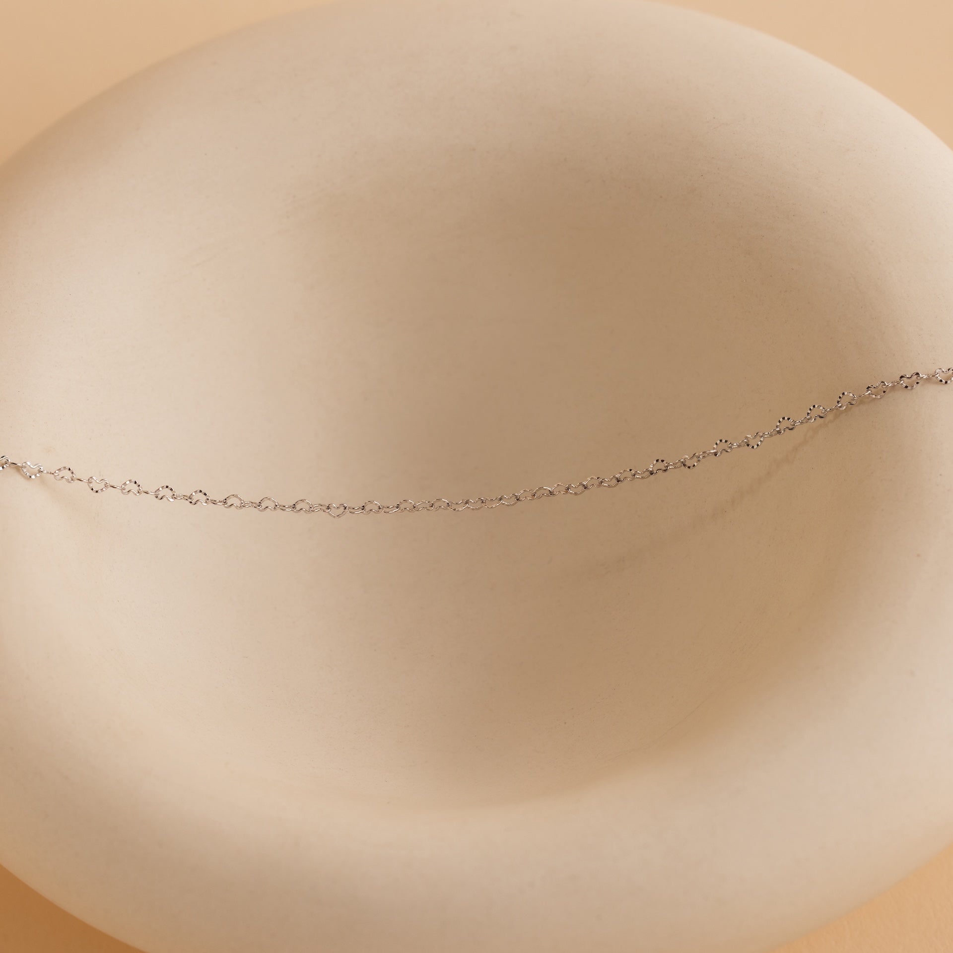 Heart Link Chain Necklace shown on a smooth, round light beige ceramic dish with a soft beige background, adding a subtle romantic touch.