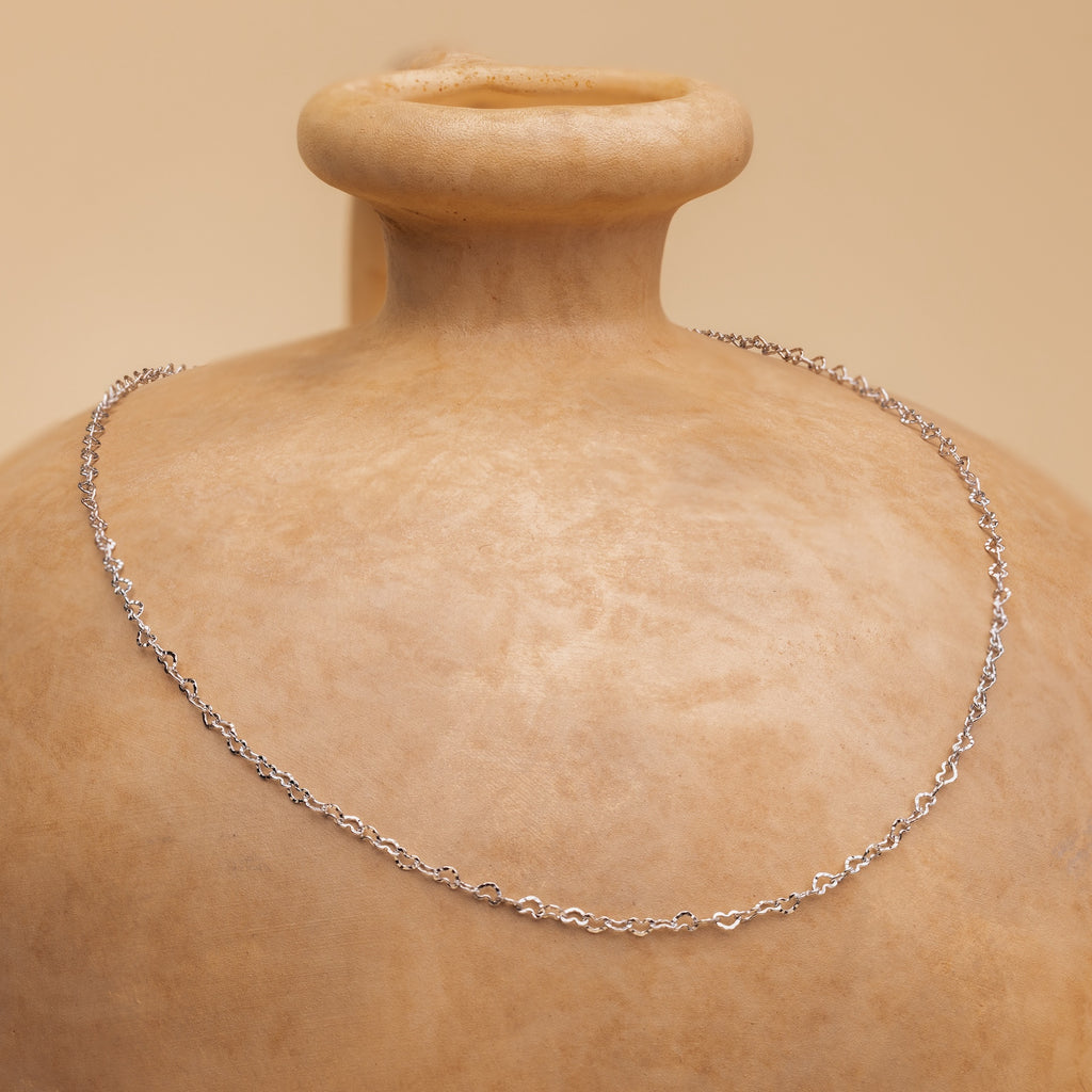 Heart Link Chain Necklace in Silver draped around the neck of a tan ceramic vase set against a beige background.