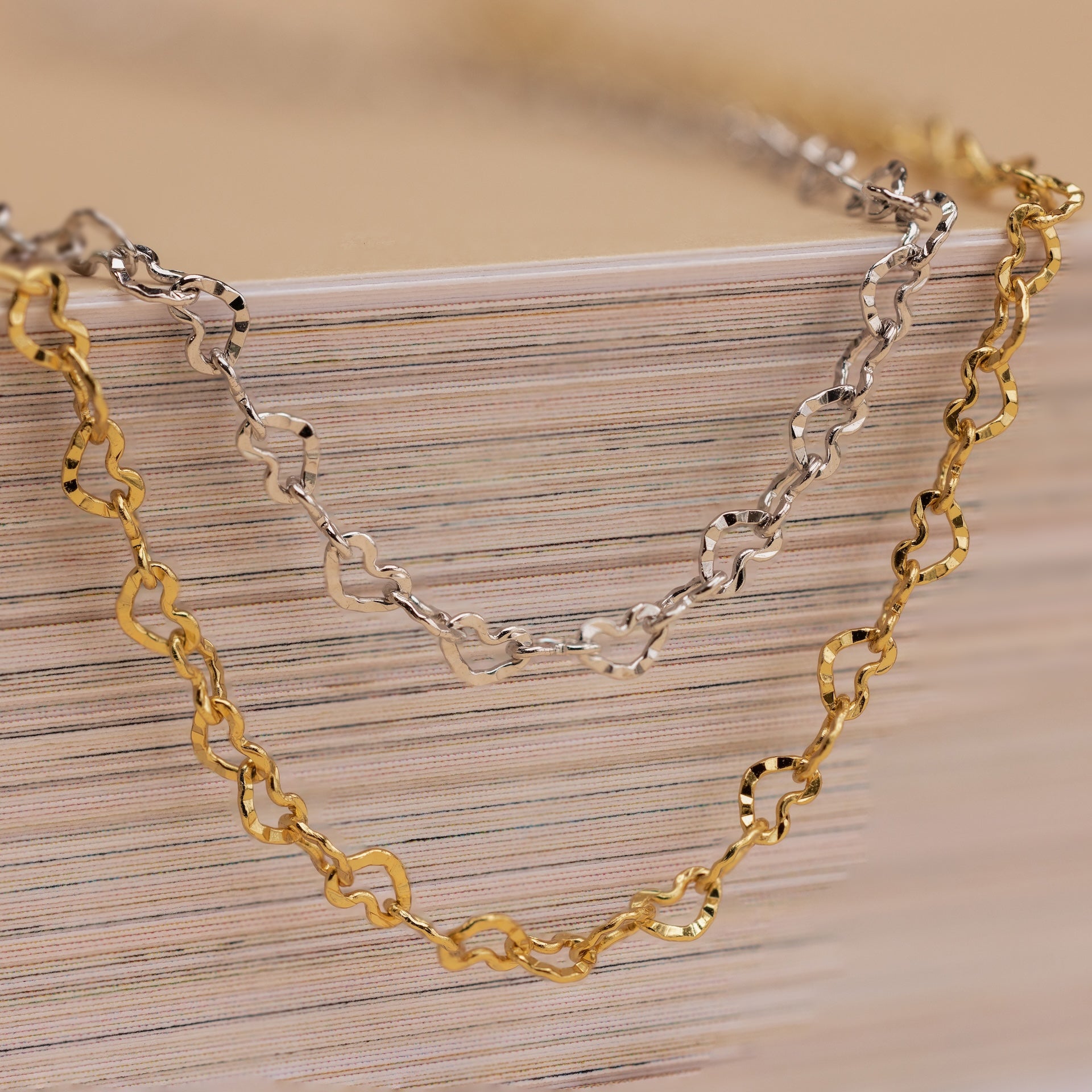 The Heart Link Chain Necklace in gold and silver features interlocking hearts, elegantly draped over a book—a romantic display perfect for heart chain lovers.