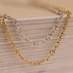 The Heart Link Chain Necklace in 18K Gold is draped over a stack of paper, adding an elegant and romantic touch to the display.