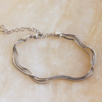 The Triple Snake Chain Bracelet in White Gold, featuring a lobster clasp, is displayed on a light beige surface—ideal for adding a layered touch to your minimal jewelry collection.