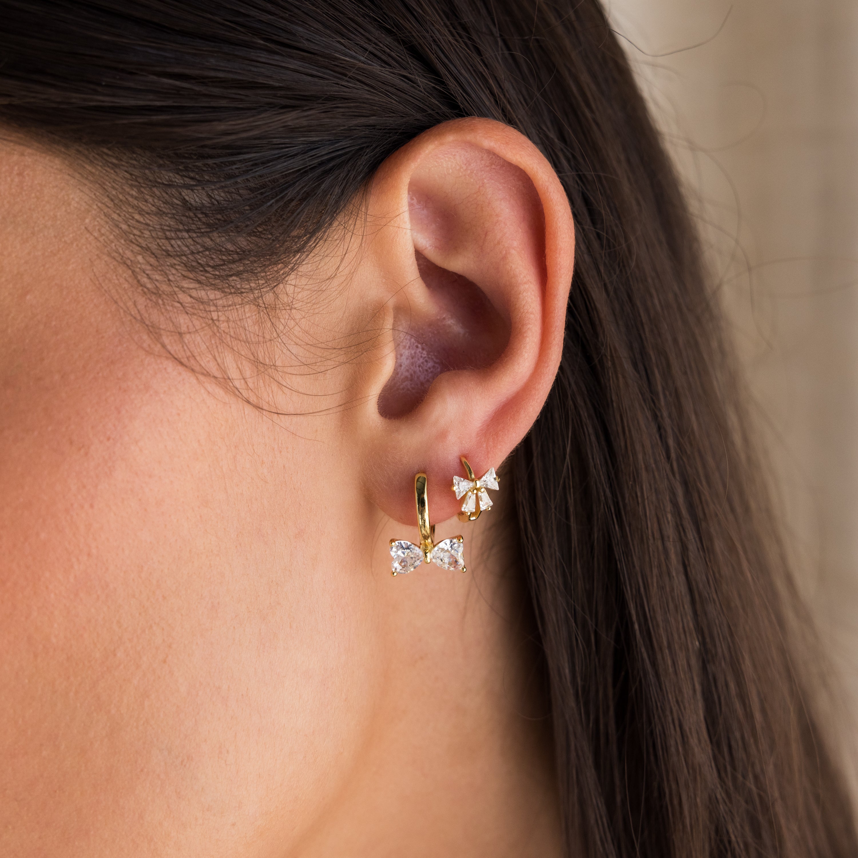 Close-up of a womans ear wearing two gold earrings: Diamond Bow Huggies and a dainty flower stud.