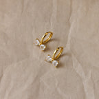 Diamond Bow Huggies: gold hoop earrings adorned with butterfly-shaped crystal charms, displayed elegantly on crumpled beige paper.