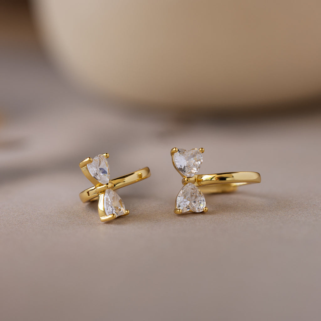 Diamond Bow Huggies featuring two vertically set pear-cut clear gemstones, displayed on a soft beige surface.