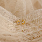The Ericka Diamond Studs, featuring a gold geometric design with small central gems, rest on soft cream lace, capturing vintage-inspired minimalist elegance.