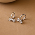 Diamond Bow Huggies: silver hoop earrings featuring bow-shaped clear gemstones. Perfect for adding chic elegance to any look for lovers of stylish bowtie earrings.