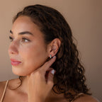 Woman with curly hair touches her Ombre Opal Huggies in Silver, gazing to the side against a neutral background.