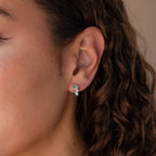 Close-up of a persons ear wearing Ombre Opal Huggies in Silver; the small turquoise and white earrings resemble teardrop gemstones, with curly hair visible.