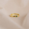 Gold ring with 'Chloe' engraving and green gemstone on a beige background