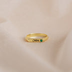 Gold ring with 'Chloe' engraving and green gemstone on a beige background