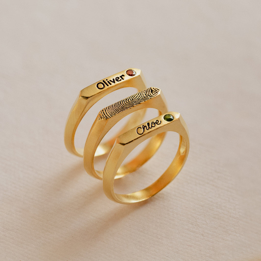 Three gold rings with engraved names on a beige background