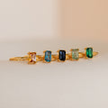 Five Emerald Cut Solitaire Rings with rectangular stones—orange, blue, dark blue, light green, and green—lined up in a row. Perfect for stacking or wearing as unique birthstone rings.