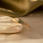 The Agate Diamond Rings Set features an Art Deco design with a green agate gemstone and rectangular clear stones, elegantly displayed on a shell against a golden fabric—an eye-catching vintage jewelry piece.