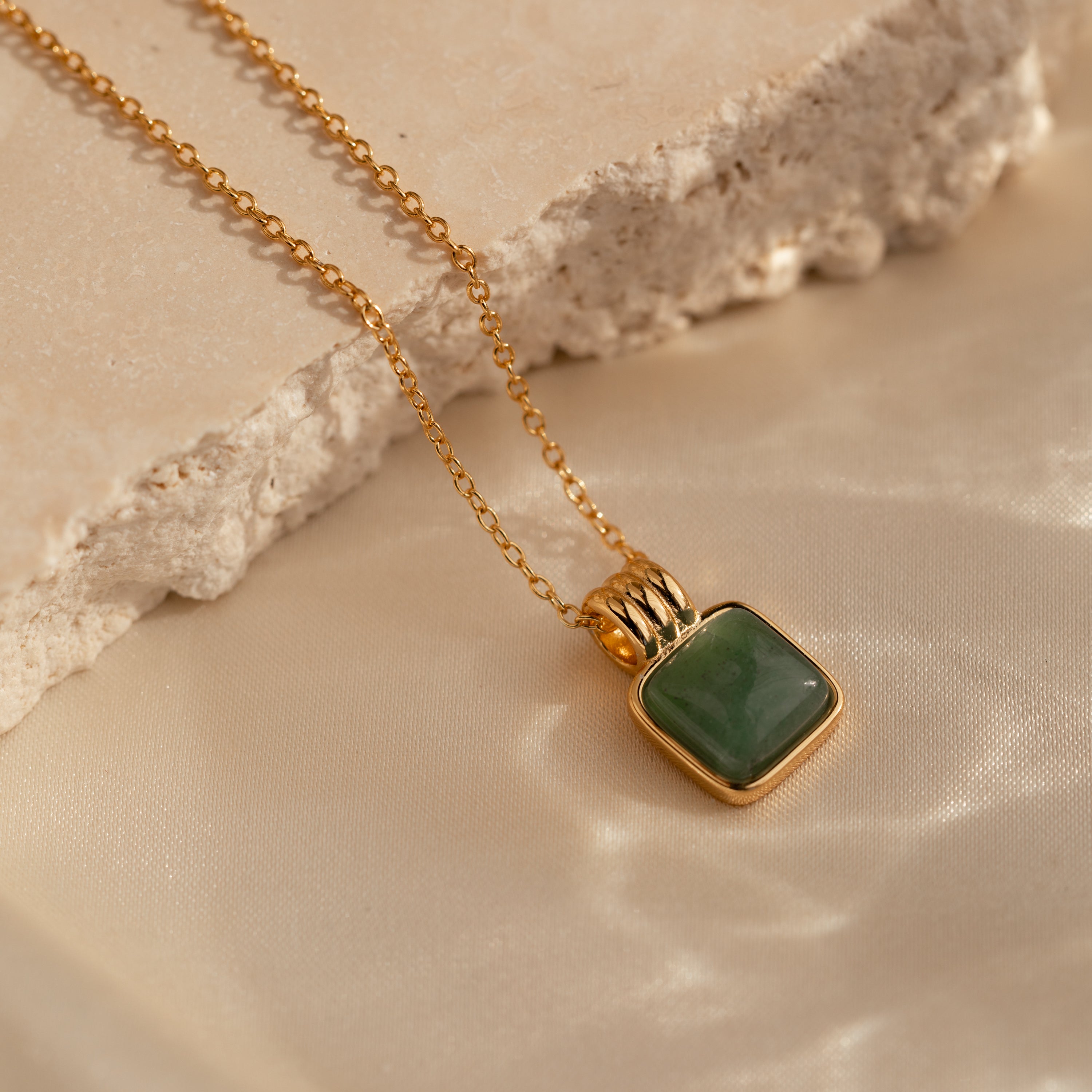 Jade Pendant Necklace with a square green jade stone symbolizing new beginnings, shown on beige fabric and a stone slab.