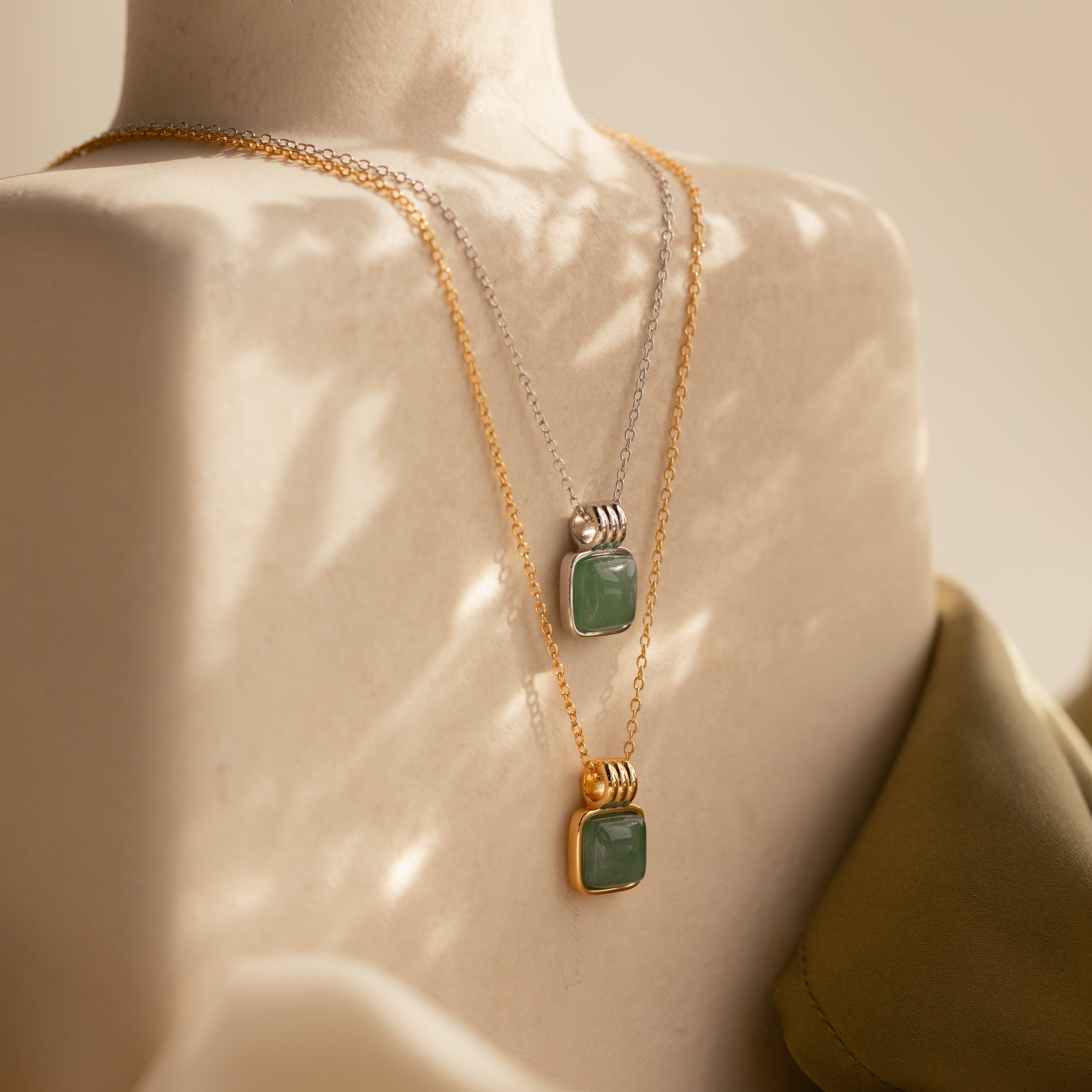 Two Jade Pendant Necklaces, one gold and one silver, featuring green jade stones symbolizing new beginnings, displayed on a mannequin under soft lighting.