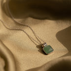The Jade Pendant Necklace in Silver, featuring a green jade stone, rests on golden fabric, exuding luck and elegance.