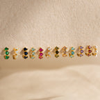 Triple Garnet Huggies, featuring vibrant garnet gemstones in a stylish huggie design, are displayed on a textured beige surface.