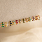 Triple Opal Huggies displayed in a row on a beige surface; these small, colorful earrings feature three opal stones each for an elegant and customizable look.