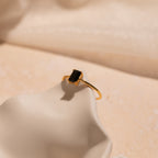 The Black Emerald Ring is a vintage-inspired gold ring featuring a rectangular black gemstone, perfect as an Art Deco piece and shown on a smooth cream-colored surface.