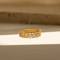 The Crystal Stacking Ring Set in 18K Gold features two rows of sparkling crystal gemstones, elegantly displayed on a sunlit surface with a neutral background—a stunning jewelry piece.