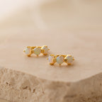Triple Opal Huggies featuring three round opals each, shown on a beige textured stone. These minimalist hoops can be customized with your preferred birthstones for a personalized accessory.